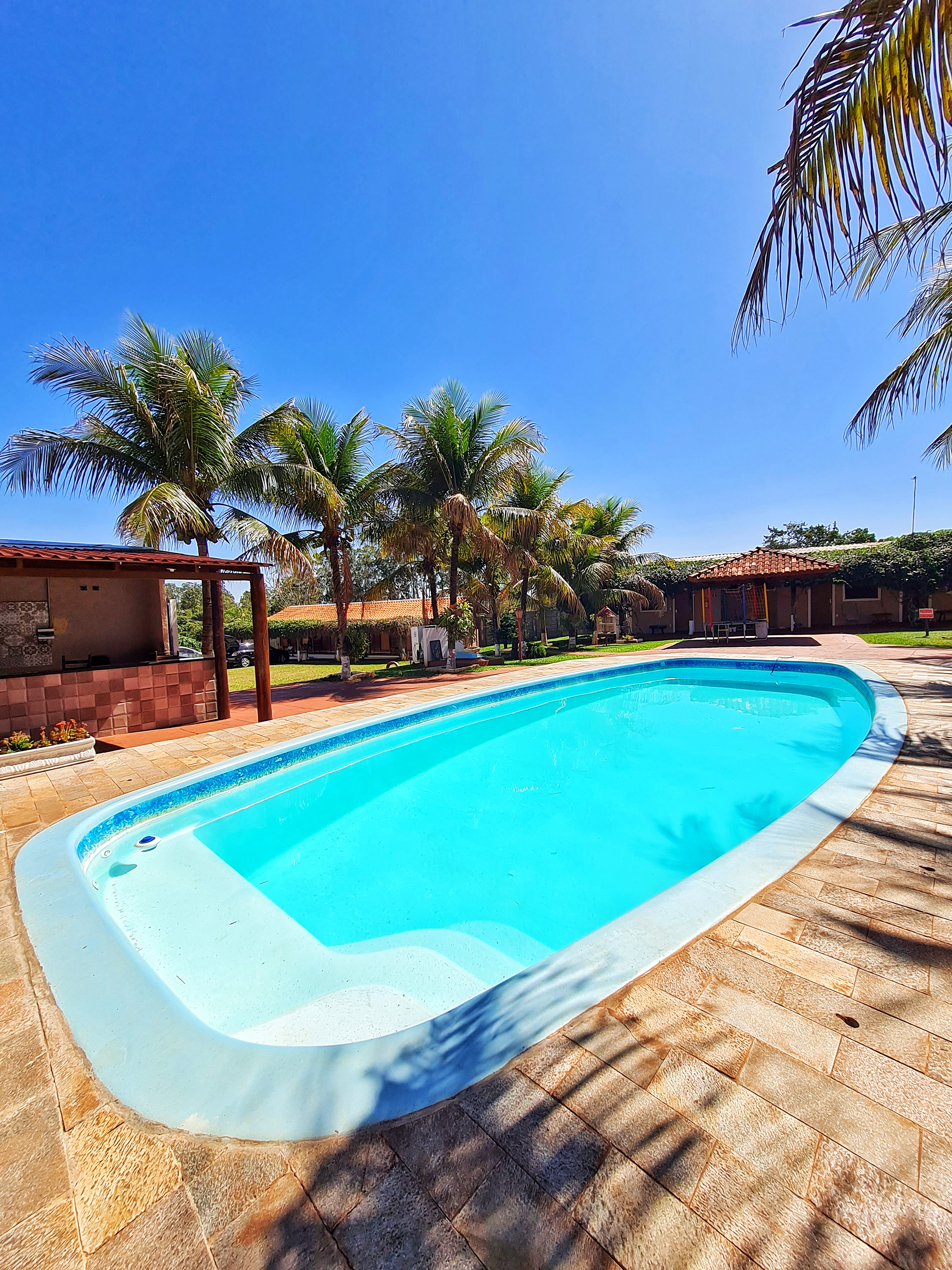 Grande piscina de águas cristalinas rodeada de coqueiros na Pousada