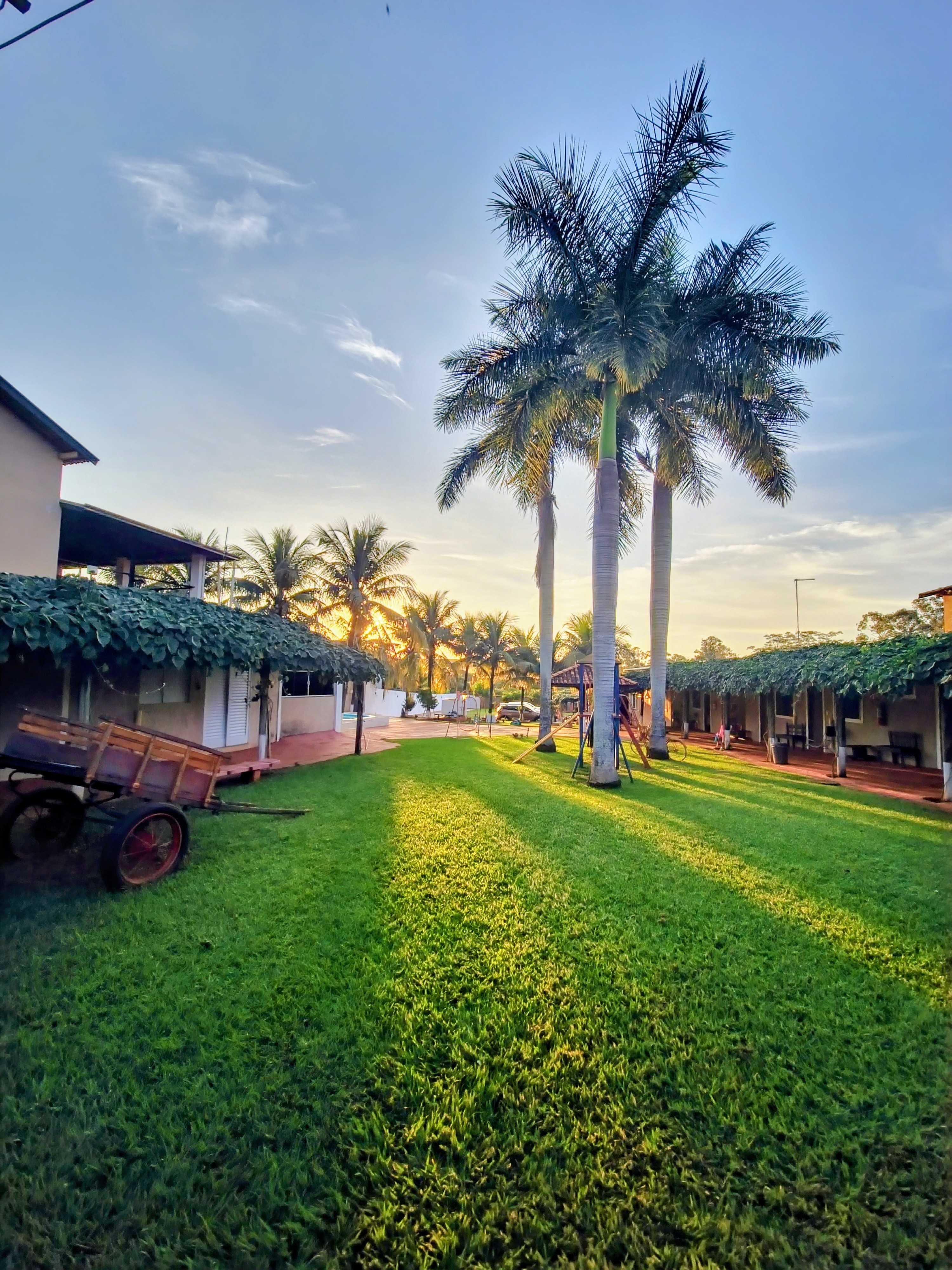 Jardim principal da Pousada Pôr do Sol sob coqueiros e o entardecer